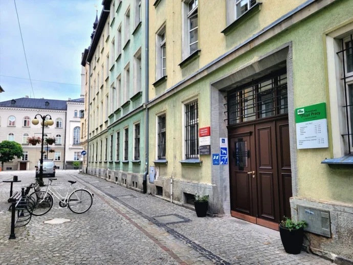 Narrow cobblestone street lined with pastel-colored buildings, a white bicycle at a bike rack, and a brown doorway.