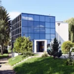 Glass-fronted office building with blue-tinted windows, open entrance, and landscaped path.