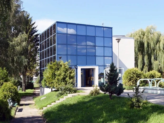 Glass-fronted office building with blue-tinted windows, open entrance, and landscaped path.