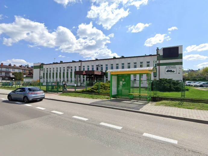 Public employment office building with white facade, green fence, and a yellow-roofed entrance on a sunny day.
