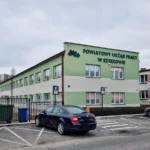 Green two-story office building with sign 'POWIATOWY URZĄD PRACY W RZESZOWIE' and parking lot in front