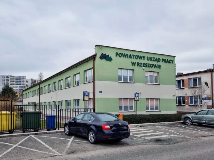 Green two-story office building with sign 'POWIATOWY URZĄD PRACY W RZESZOWIE' and parking lot in front