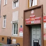 Building entrance on a pink stucco building with many red signs above the door and a Polish eagle emblem