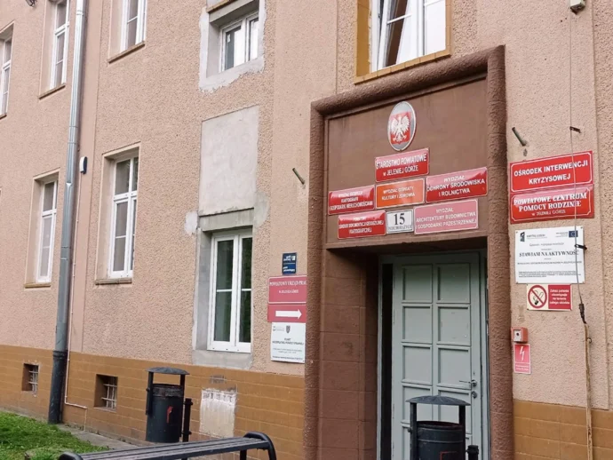 Building entrance on a pink stucco building with many red signs above the door and a Polish eagle emblem