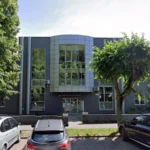 Front view of a modern office building with a curved glass facade and a sign reading 'Powiatowy Urząd Pracy' above the entrance, trees and parked cars in front.