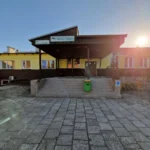 Front of a public employment office (Urząd Pracy) with a yellow and brown exterior, a dark canopy over the entrance, stairs and a ramp leading to the doors, sunny day with sun flare to the right.