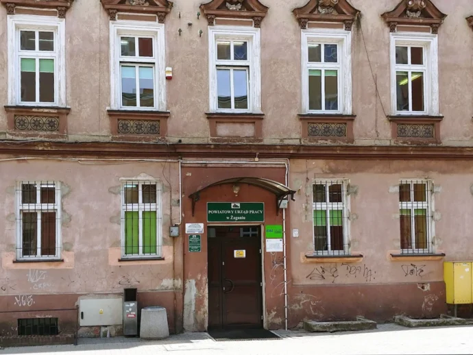 Old pink building with six upper windows and a central door labeled Powiatowy Urząd Pracy w Żaganiu.