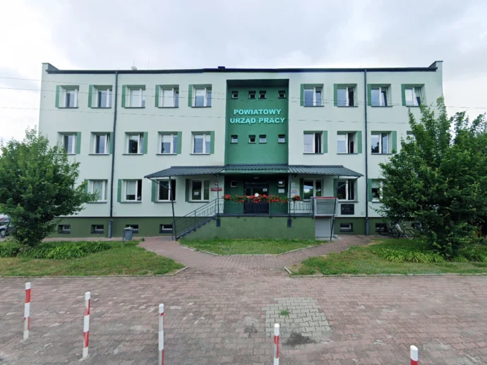 Public employment office building in Poland with a green center section and red flower boxes at the entrance