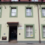 Facade of a pale green building with green window frames; entrance marked Urząd Pracy (employment office) in Poland.