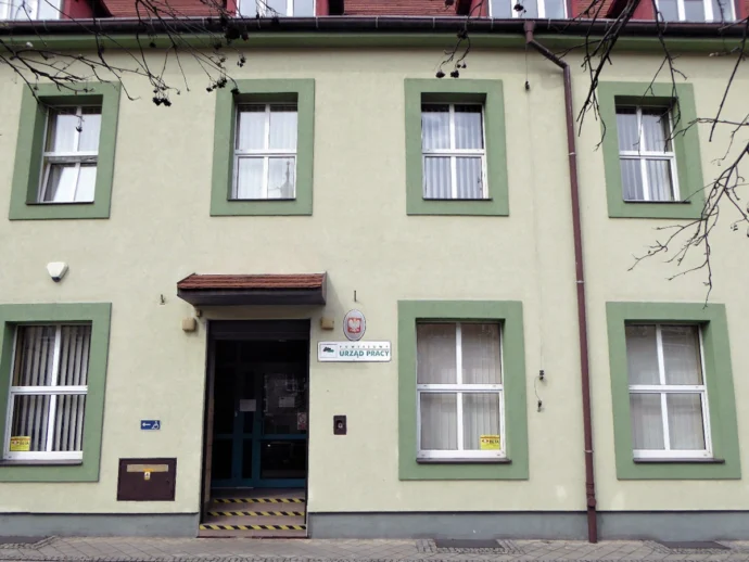 Facade of a pale green building with green window frames; entrance marked Urząd Pracy (employment office) in Poland.
