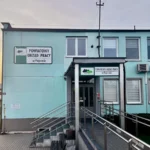 Turquoise two-story office building with signs reading 'Powiatowy Urząd Pracy w Pajęcznie' and a ramp with metal handrails at the entrance.